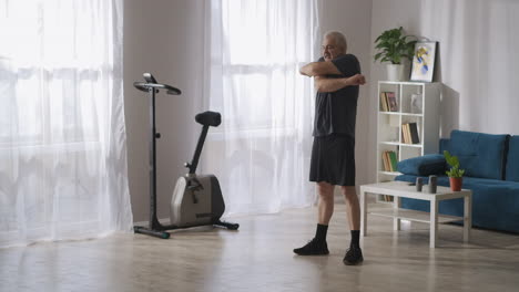 Un-Hombre-Adulto-De-Mediana-Edad-Está-Entrenando-Solo-En-Su-Apartamento-Por-La-Mañana-Agitando-Las-Manos-Calentando-Los-Músculos